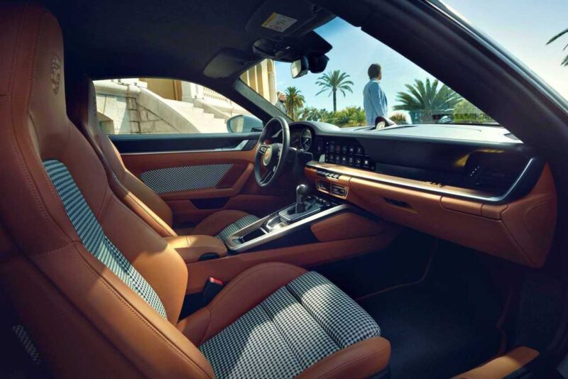 Interior of a luxury sports car with brown leather and houndstooth seats, manual transmission—a scene reminiscent of a Porsche 911 Comparison: 997 Sport Classic vs 992 Sport Classic—with a man standing outside near palm trees.