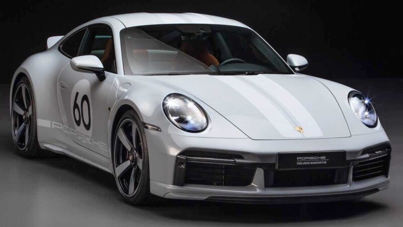 A silver Porsche 911 sports car with the number 60 on the door, white racing stripes, and distinctive alloy wheels is displayed in a studio setting—perfect for a Porsche 911 Comparison: 997 Sport Classic vs 992 Sport Classic.