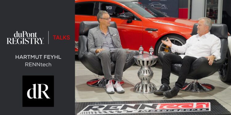 Two men in conversation sit in chairs with a table between them, a red AMG car in the background, and duPont REGISTRY and RENNtech branding displayed.