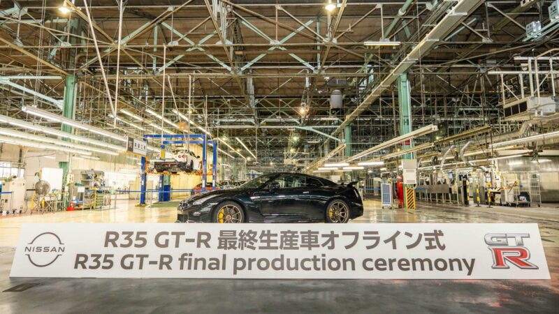 A black Nissan R35 GT-R is displayed in a factory behind a sign that reads, “R35 GT-R final production ceremony,” in English and Japanese, marking the end of an era for this iconic model.