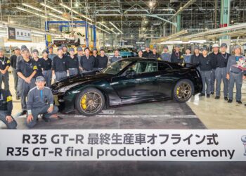 A group of factory workers poses with the last Nissan R35 GT-R beside a sign reading "R35 GT-R final production ceremony," marking the end of an era inside an automotive assembly plant.