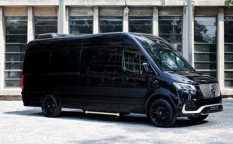 A black Mercedes-Benz Sprinter van, a true example of unique garage creation, is parked outside in front of a building with large windows.