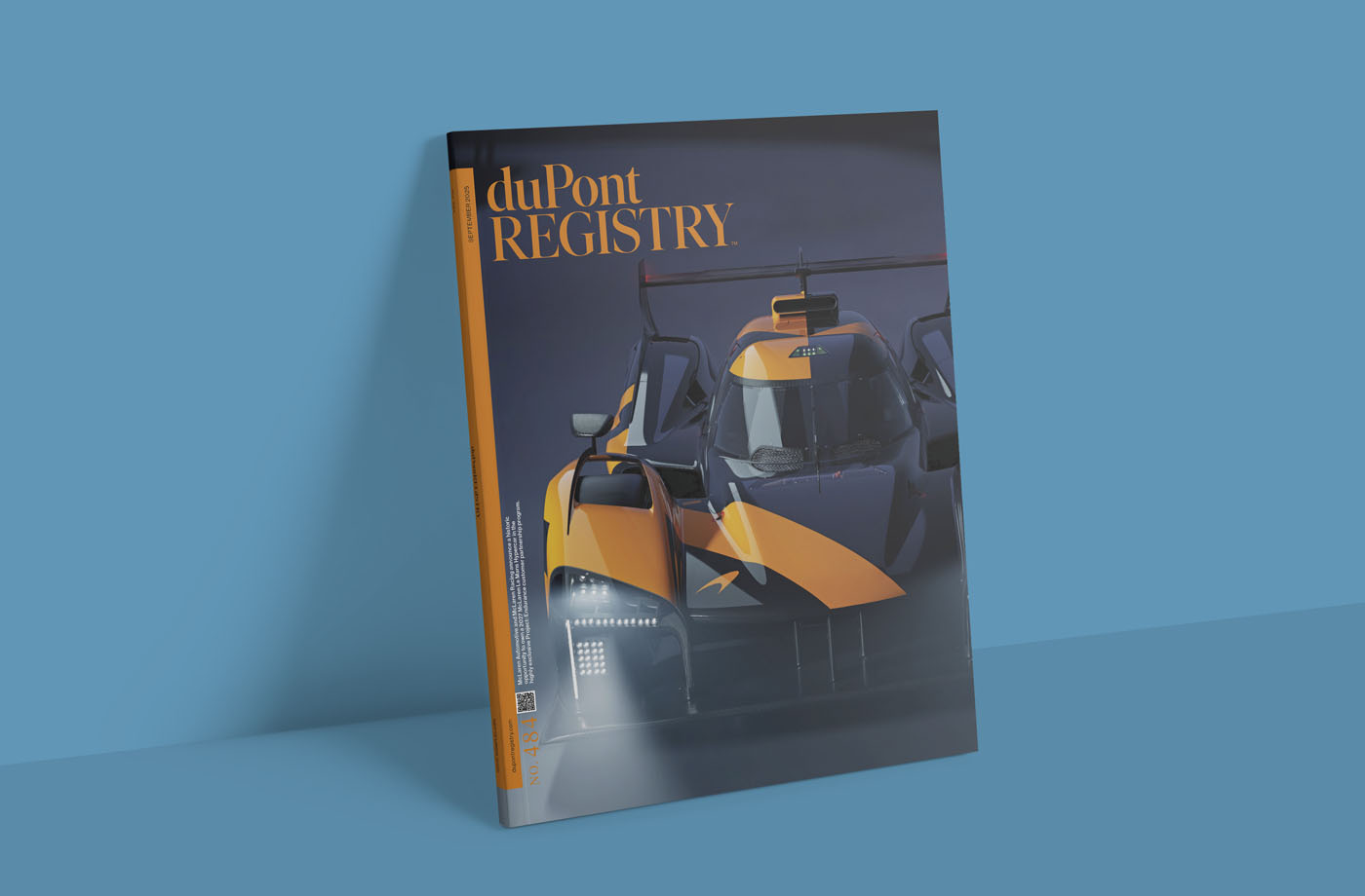 A duPont REGISTRY magazine from September 2025 stands upright against a blue wall, featuring a yellow and black sports car on the cover.