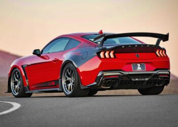 A red Ford Mustang Shelby GT500 is parked on a road, viewed from the rear three-quarter angle, inspired by the Shelby American Debuts 2026 Wide Body Super Snake-R, an 850+ HP track weapon with coil suspension and a large rear wing.