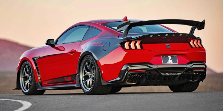A red Ford Mustang Shelby GT500 is parked on a road, viewed from the rear three-quarter angle, inspired by the Shelby American Debuts 2026 Wide Body Super Snake-R, an 850+ HP track weapon with coil suspension and a large rear wing.