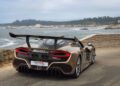 A brown Hennessey Venom F5 sports car boasting 1,817HP is parked near a stone wall, overlooking the ocean with a rocky coastline and trees in the background.