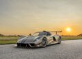 A metallic Hennessey Venom F5 sports car with a large rear wing is parked on a paved road at sunset, surrounded by grassy fields and a clear sky, showcasing its impressive 1,817 HP and manual transmission.