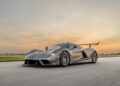 A silver Hennessey Venom F5 with a large rear wing drives on an open road at sunset, showcasing its 1,817 HP power against fields and a clear sky in the background.