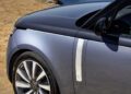 A close-up of the front left side of a silver Range Rover SV parked on dry grass near a rocky shoreline at Asilomar, with the ocean visible in the background during Monterey Car Week.