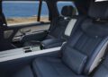 The image shows the luxurious back seats of a one-off Range Rover SV Asilomar with blue leather upholstery, foldable trays, and a view of the ocean through the window—an exclusive sight at Monterey Car Week.