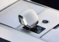 Close-up of a modern car’s central console featuring a white gear shift lever, visible drive mode indicators, and an engine start-stop button—capturing luxury details worthy of Monterey Car Week.