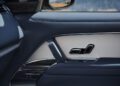 Close-up of a car’s interior passenger door and side mirror, possibly from a one-off Range Rover, with a view of water and a blurry landscape outside—evoking the scenic routes of Monterey Car Week.
