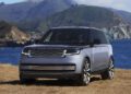 A silver Range Rover SV SUV parked on dry grass with mountains and the blue ocean in the background at Asilomar during Monterey Car Week.