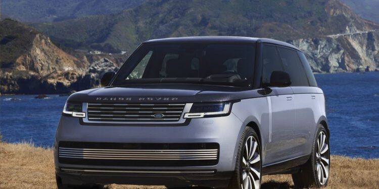A silver Range Rover SV SUV parked on dry grass with mountains and the blue ocean in the background at Asilomar during Monterey Car Week.