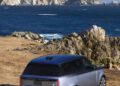A silver Range Rover SV is parked on dry grass at Asilomar near rocky cliffs overlooking the ocean, with mountains in the background—capturing the spirit of Monterey Car Week.