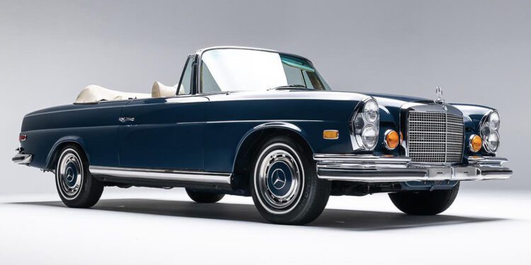 A classic dark blue convertible car with chrome accents and a beige interior, photographed in a studio setting against a plain gray background, ready to shine at the Auburn Auction by Worldwide Auctioneers.