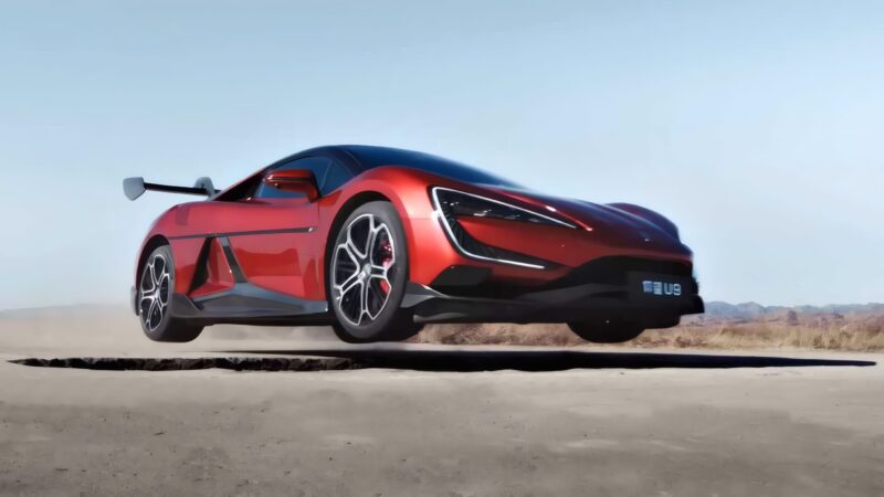 A red sports car, reminiscent of BYD’s YangWang U9 Track Edition that just hit 472 km/h setting a new EV top-speed record, is airborne above a cracked desert road with its wheels off the ground and a dust trail behind it.