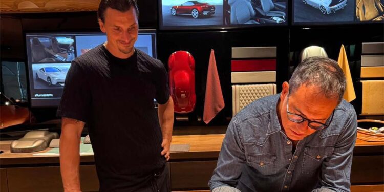 Two men are in a design studio; one sketches a car on paper while the other observes. Behind them, images of the Ferrari F80 and materials are displayed—echoing the creative spirit of Flavio Manzoni.