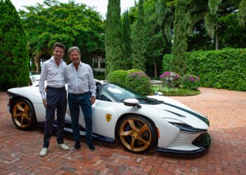 Two men stand smiling next to a white Ferrari sports car with gold wheels, parked on a brick driveway surrounded by greenery—an elegant scene reminiscent of a fine art collection.