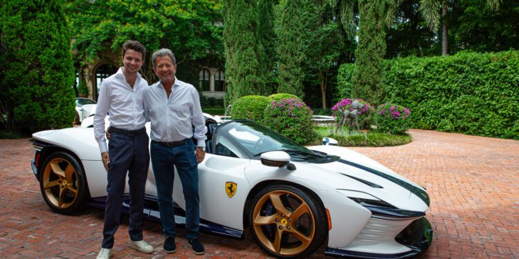 Two men stand smiling next to a white Ferrari sports car with gold wheels, parked on a brick driveway surrounded by greenery—an elegant scene reminiscent of a fine art collection.