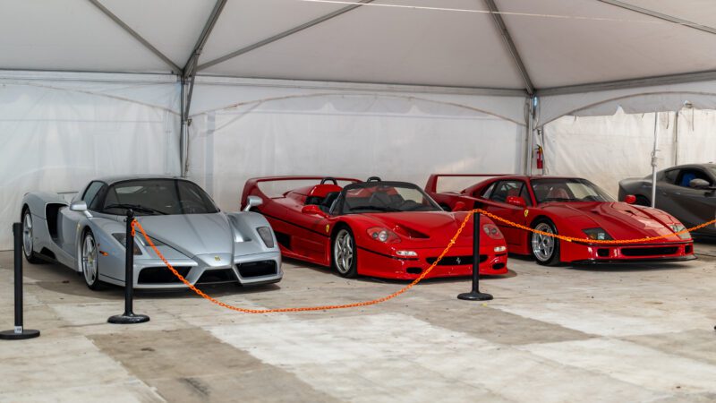 Three Ferrari sports cars—a silver Enzo, a red F50, and a red F40—are displayed under a white tent behind an orange chain barrier at Cars on 5th, part of the renowned duPont REGISTRY Events.