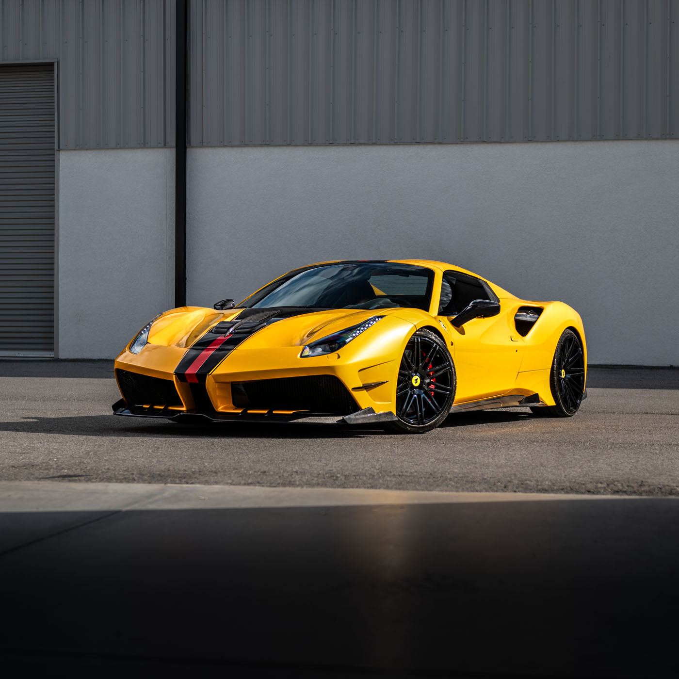 A yellow sports car with black and red racing stripes is parked on a paved surface in front of an industrial building, ready to turn heads at the Exotic Car Show in St. Armands Circle, Sarasota.