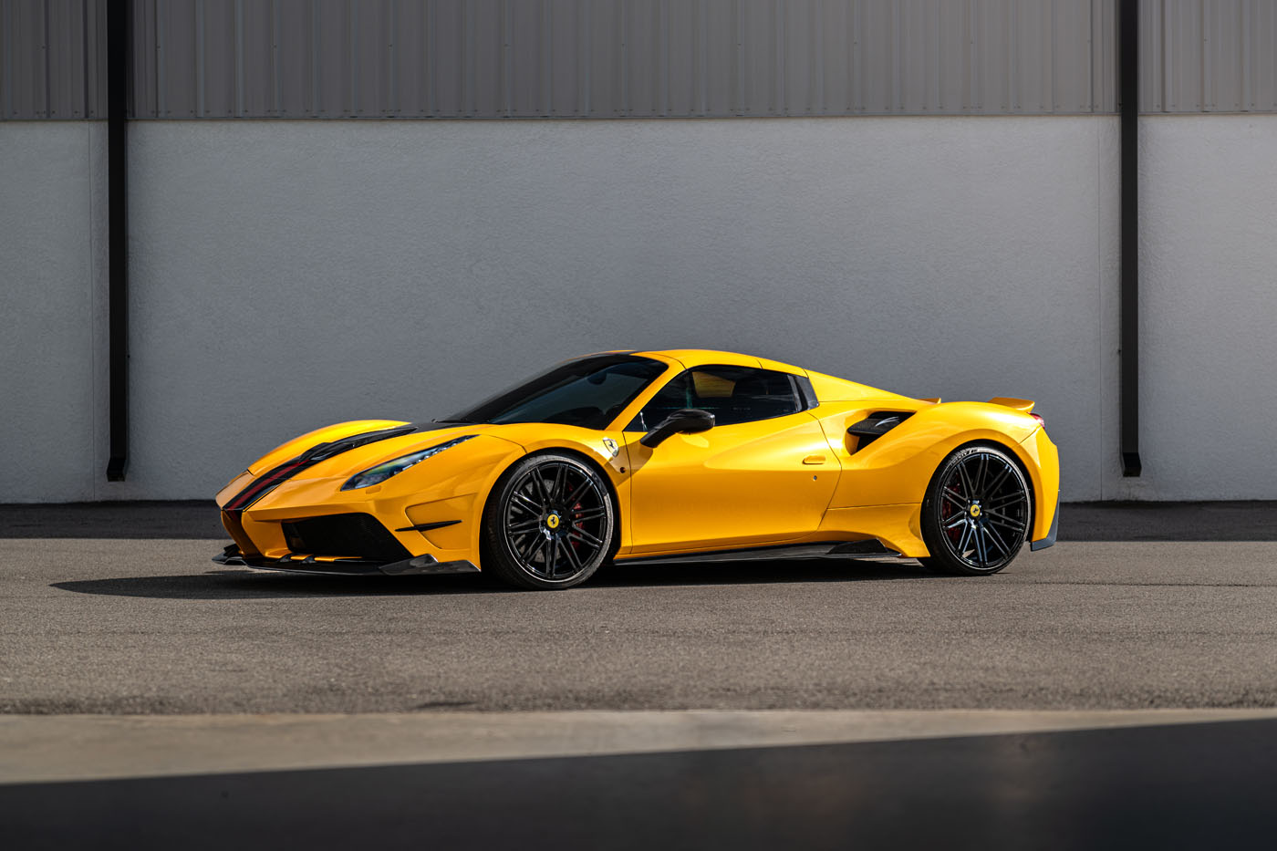 A yellow sports car with black rims is parked on a paved surface in front of a white and gray industrial building at the Exotic Car Show in Sarasota.