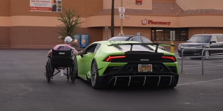 Garet Thomas, in a wheelchair, moves toward a green Lamborghini parked in a pharmacy lot during Monterey Car Week 2025. A "We're Hiring" sign is visible on the building in the background.
