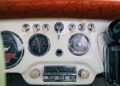 Close-up of a vintage car dashboard showing speedometer, gauges, push-button controls, and a radio, with a brown patterned top section visible.