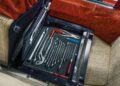 A set of hand tools neatly organized in a compartment under a car seat with red and beige upholstery.