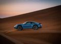 A blue Porsche sports car parked on sand dunes at sunset under a clear sky, featured in the Sonderwunsch video series.