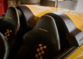 Close-up of two black leather Porsche car seats with yellow checkered patterns and "Speedster" embroidered on the headrests, inside a yellow convertible sports car—part of the Sonderwunsch video series.