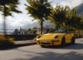 A yellow Porsche convertible sports car drives along a tree-lined road beside a lake with mountains in the background, capturing the spirit of Sonderwunsch in this stunning video series moment.