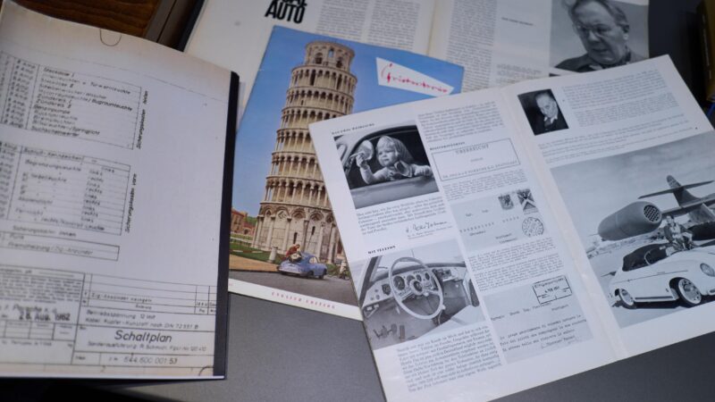 A collection of open magazines and documents on a table, featuring car schematics, photos, and articles, including an image of the Leaning Tower of Pisa.