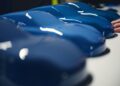 Several glossy blue Porsche car model shells are lined up on a white surface, with a person's hand touching one—perhaps part of a Sonderwunsch project or video series exploring custom automotive design.