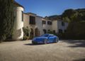 A blue Porsche sports car is parked on a gravel driveway in front of a large, cream-colored villa with arched entry and tall windows, surrounded by trees and greenery under a clear sky—capturing true Sonderwunsch elegance.