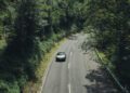 A Porsche glides along a winding, tree-lined road surrounded by lush greenery on both sides, capturing the spirit of Sonderwunsch in this video series.