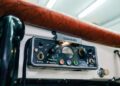 Close-up of a vintage Lorenz radio communication device with several dials, switches, and indicator lights, mounted below a brown patterned dashboard.