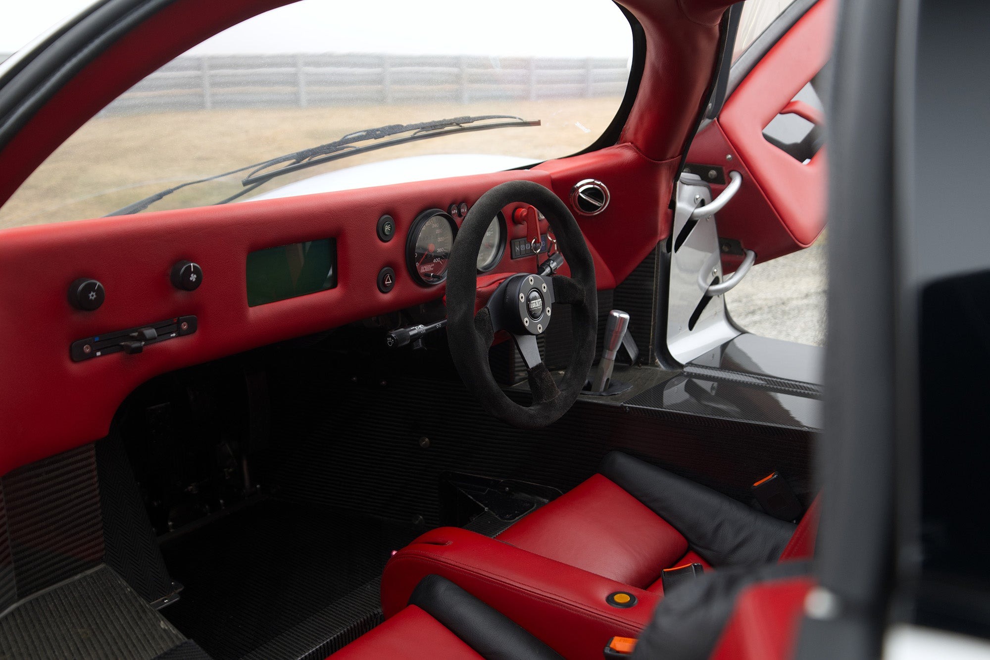 The image shows the interior of a Lotec C1000 sports car with red leather seats, a red dashboard, a racing-style steering wheel, and carbon fiber accents—perfect for any Petrolicious Film Friday feature.
