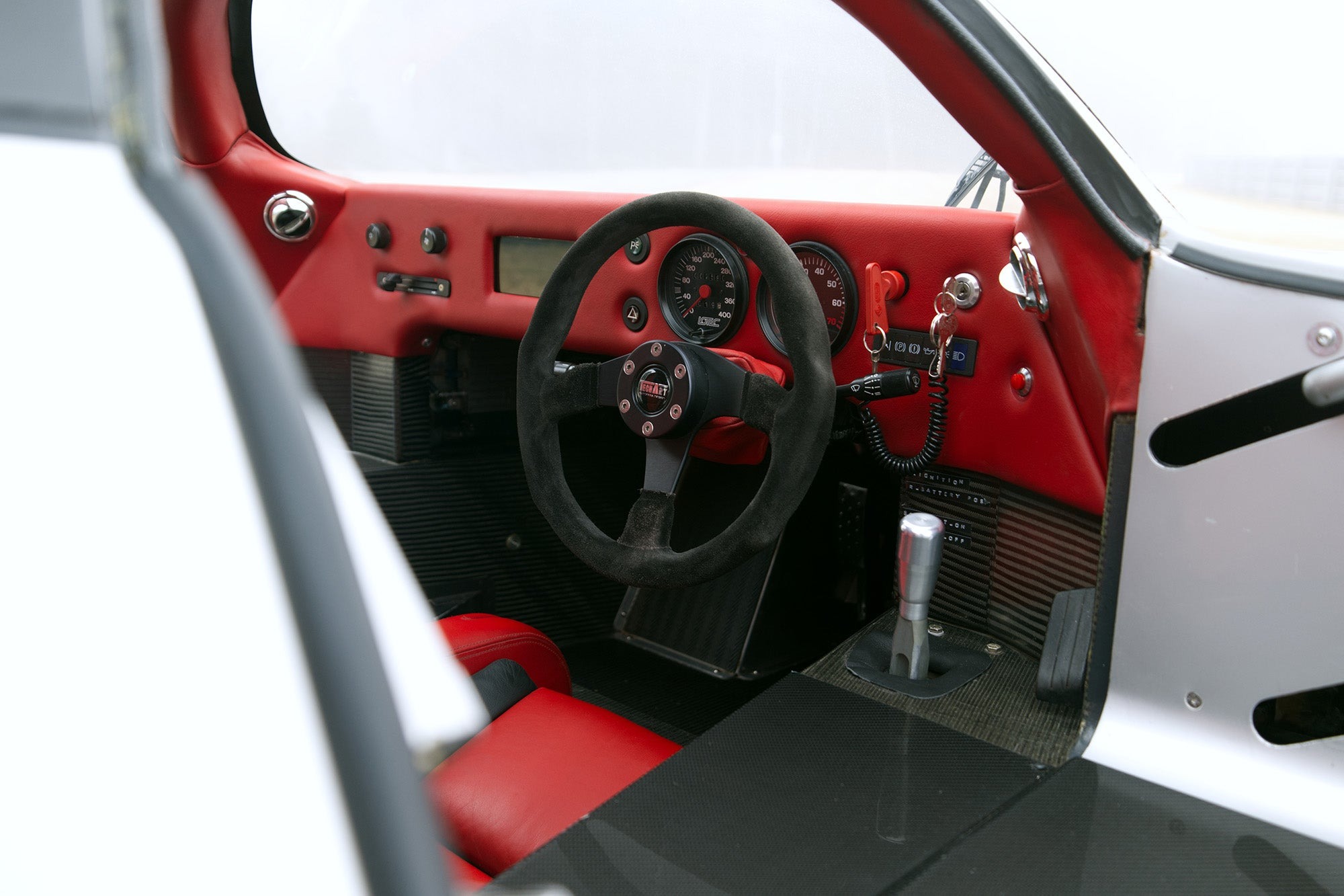 Interior view of a Lotec C1000 sports car featuring a black steering wheel, red and black dashboard, analog gauges, gear shifter, and red leather seats—perfect for any Petrolicious Film Friday enthusiast.