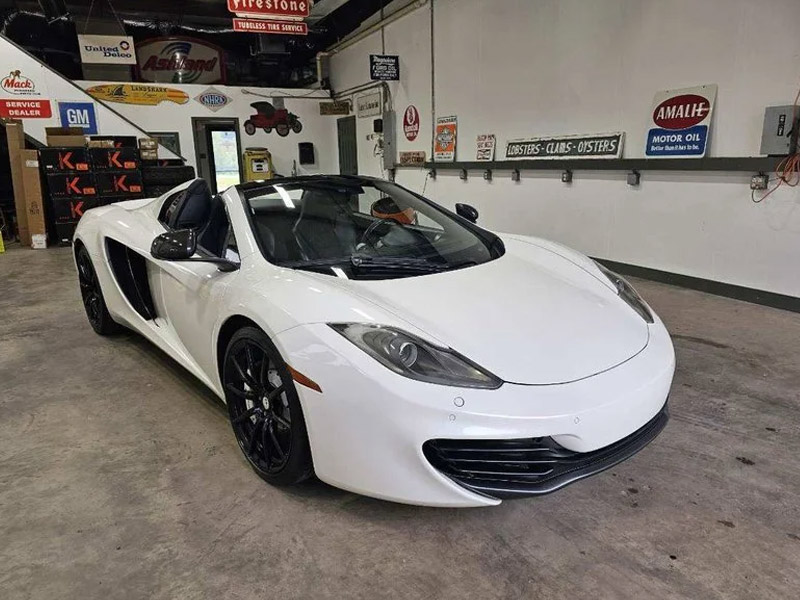 A white convertible sports car with black wheels is parked inside a garage filled with automotive signs and equipment, ready to impress at the Fall Carlisle Collector Car Auction.
