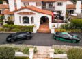 Aerial view of a large white house with a red-tiled roof, surrounded by greenery, with two black Rimac electric hypercars parked in the driveway—perfect for Monterey Car Week.