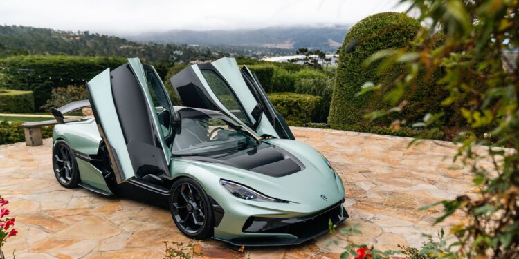 A light green Rimac electric hypercar with its butterfly doors open is parked on a stone driveway surrounded by greenery and flowers, reminiscent of an exclusive Monterey Car Week showcase.