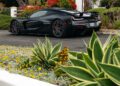 A black Rimac luxury sports car, inspired by Electric Hypercars seen at Monterey Car Week, is parked on a suburban street near a house with a red-tiled roof and lush landscaping.
