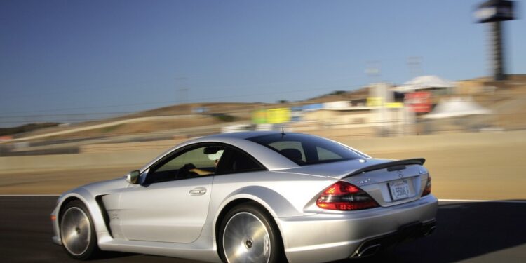 A silver sports car drives on a racetrack, with blurred background indicating motion and a clear sky above.