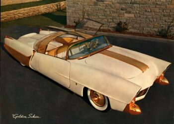 The Golden Sahara II, a vintage white and gold convertible with a transparent roof, is parked on a driveway near a stone wall.
