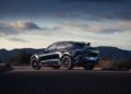 A 2026 Aston Martin DBX S First Drive: The Best Super SUV Gets Even Better is parked on a paved road with hills and trees in the background under a cloudy sky.