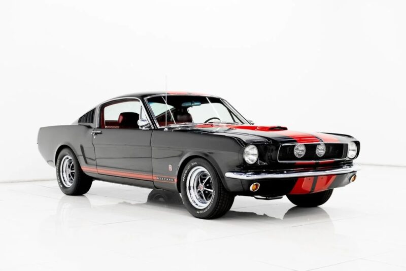 A classic black Ford Mustang Fastback with red racing stripes is parked in a white studio, viewed from the front left angle—a true icon among Classic Muscle Cars.
