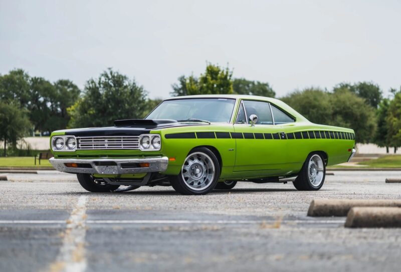 A bright green, vintage two-door muscle car with black racing stripes is parked in an empty outdoor lot on a cloudy day—an eye-catching choice for fans of classic cars.