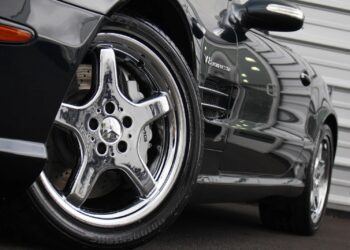 Close-up view of a luxury Mercedes-Benz sports car, focusing on a shiny chrome wheel and part of the front fender, parked near a metal-clad building.